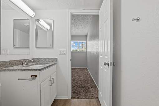 A bathroom with a sink, mirror, and a door leading to another room.
