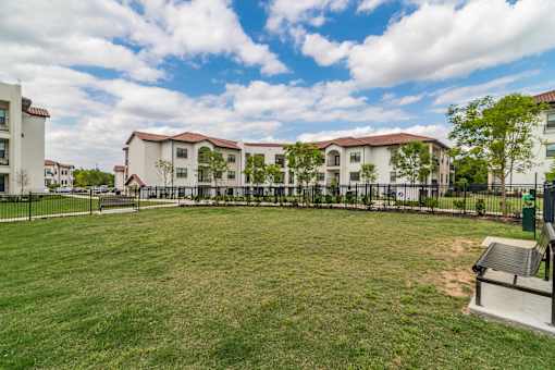 A grassy field with a bench and apartment buildings in the background.