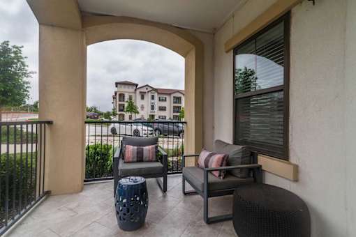 A balcony with a chair and a sofa with a view of a building in the background.