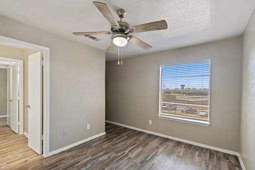 A room with a ceiling fan and a window overlooking a parking lot.