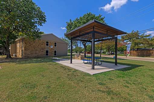 A pavilion with a picnic table is situated in a grassy area.