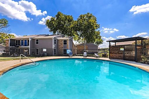A swimming pool in front of a building with a blue sky and clouds in the background.