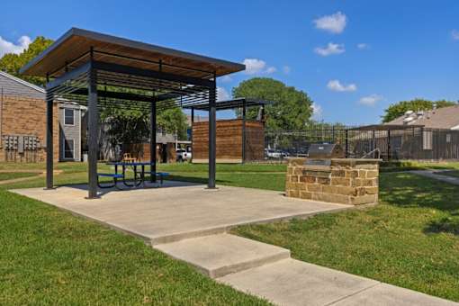 A pavilion with a picnic table is situated in a grassy area.