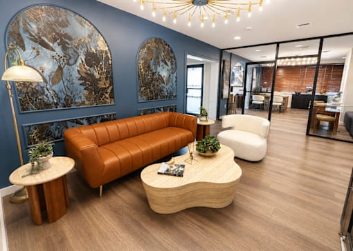 A modern living room with a brown leather sofa, a wooden coffee table, and a large abstract painting on the wall.
