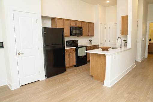 A black refrigerator is in the corner of a kitchen with wooden cabinets.