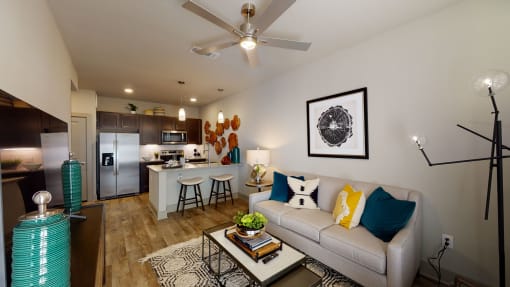 a living room with a couch and coffee table in front of a kitchen with a breakfast bar
