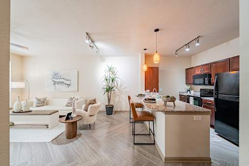 A modern kitchen and living room with a white couch, wooden coffee table, and a potted plant.