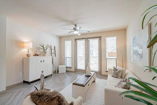 A living room with a white couch, a brown rug, a wooden coffee table, a white cabinet, a ceiling fan, and a large painting on the wall.