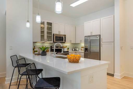 A kitchen with white cabinets and a white countertop with a basket of fruit on it.