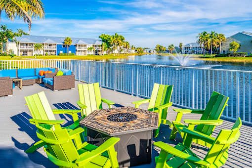A table surrounded by green chairs is in the foreground of a sunny patio.