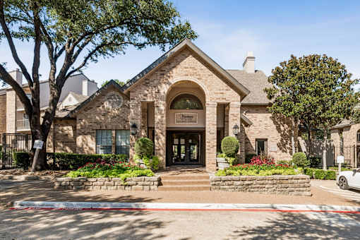 A building with a stone facade and a sign that reads "Ladies' Manor" is surrounded by trees and flowers.