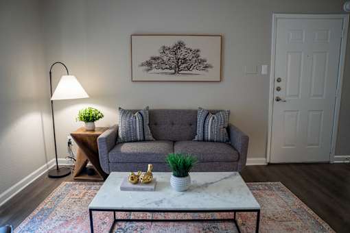 A living room with a grey couch, a white coffee table, and a painting on the wall.