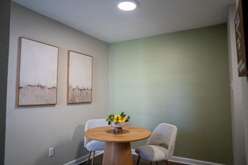 A dining room with a table and chairs and two paintings on the wall.