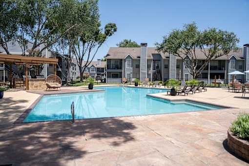 A large swimming pool surrounded by a patio and trees.