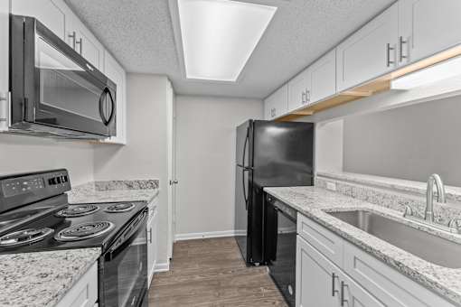 A black refrigerator stands in a kitchen with granite countertops and stainless steel appliances.
