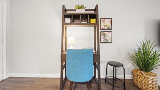 a desk with a blue chair and a black stool in a room with a white wall and