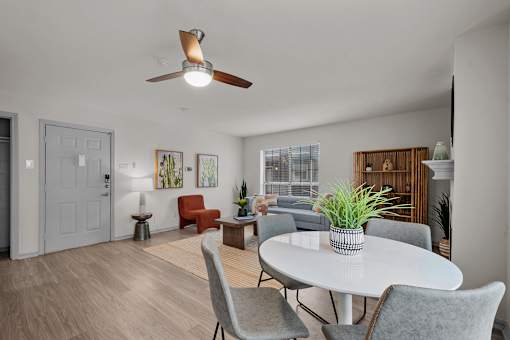A living room with a white ceiling fan and a white table with grey chairs.