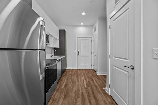 A modern kitchen with a refrigerator on the left and a wooden floor.