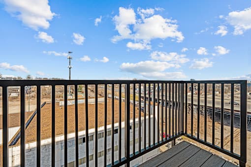 A balcony with a black railing and a view of a train track and a building.
