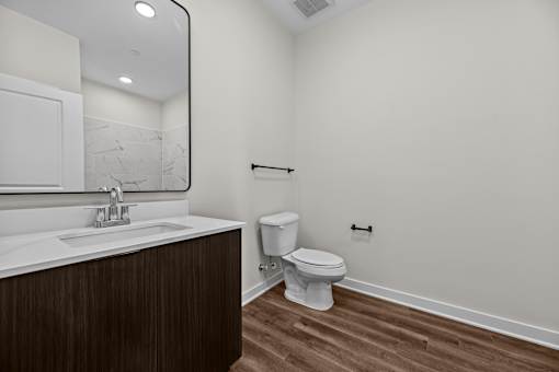 A white toilet sits in a bathroom with a wooden vanity and marble counter.