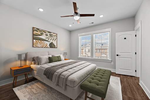 A bedroom with a large bed, a green ottoman, and a ceiling fan.
