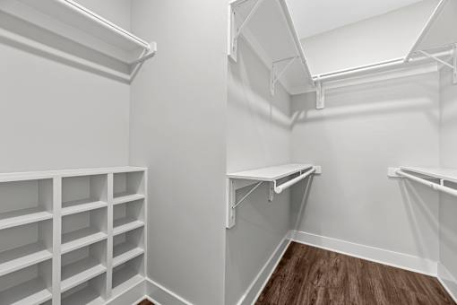 A white walk-in closet with shelves and a wooden floor.
