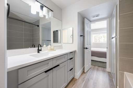 A bathroom with a sink, mirror, and a door leading to a bedroom.
