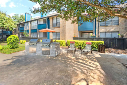 a patio with a grill and chairs in front of an apartment building