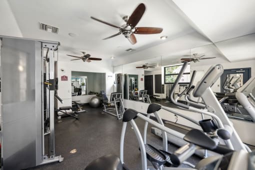 a gym with cardio equipment and a ceiling fan