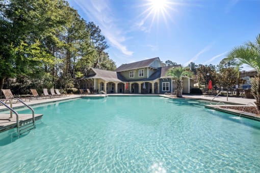 A large swimming pool in front of a house with a sunny sky above.