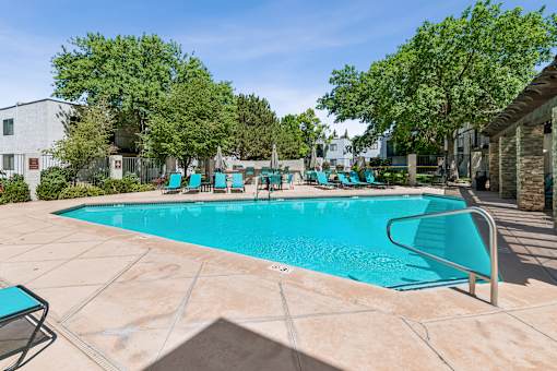 A swimming pool surrounded by trees and chairs.