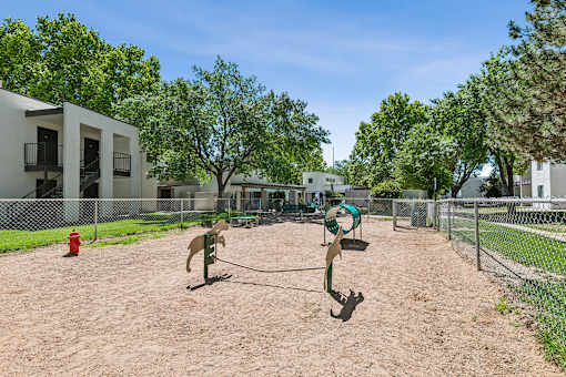 A dog park with a sandy area and a green exercise equipment.