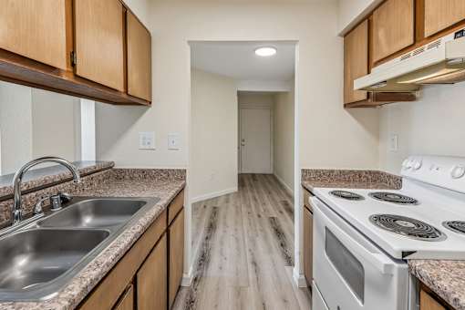 A kitchen with a stove, sink, and wooden cabinets.