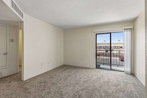 A room with a carpeted floor, a sliding glass door, and a white door.
