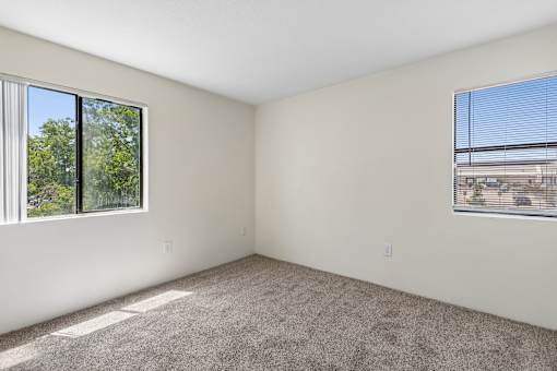 A room with a carpeted floor and two windows.