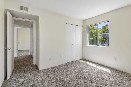 A room with a carpeted floor, a window, and a door leading to another room.