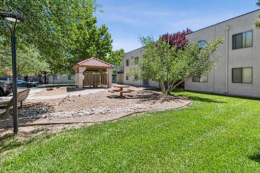 A gazebo sits in the middle of a grassy area in front of a building.