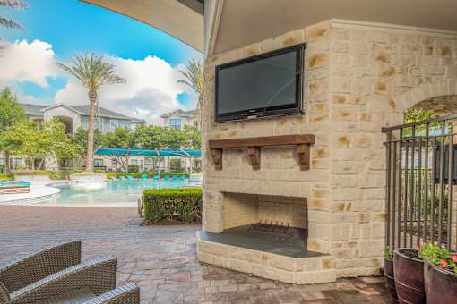 A patio with a stone fireplace and a television mounted on the wall.