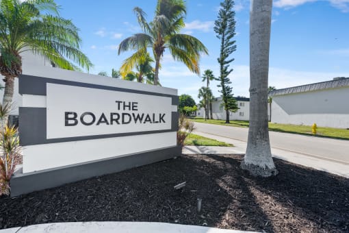 a sign for the boardwalk on the side of a road with palm trees
