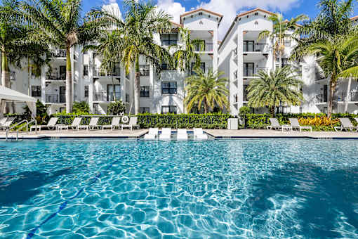 A swimming pool in front of a white building with palm trees.