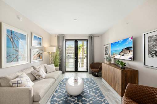 A modern living room with a white sofa, a TV, and a large window with curtains.