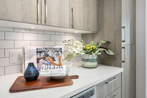 A kitchen counter with a bowl, vase, and magazine on it.