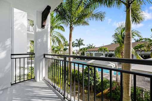 A balcony with a black railing and a pool in the background.