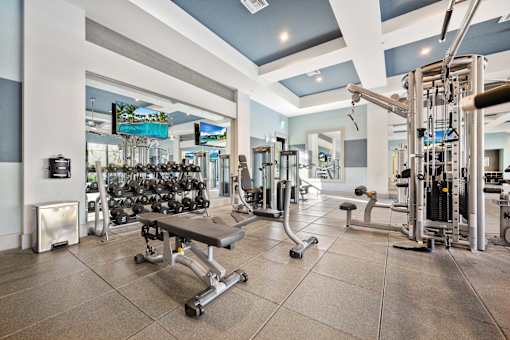 A gym with a variety of equipment including dumbbells, weight machines, and a bench.