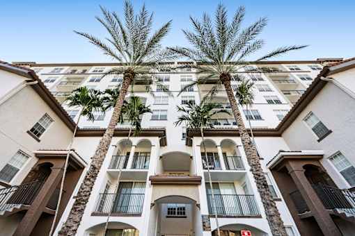 A tall building with balconies and palm trees in front.