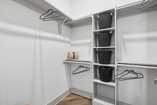 A white closet with clothes hanging and baskets on shelves.
