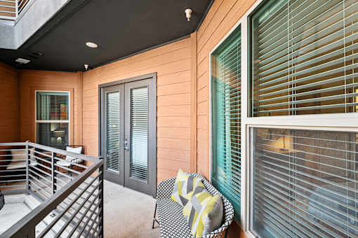 A chair with a yellow and grey blanket is in front of a window with blinds.