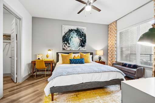 A bedroom with a bed, a chair, a painting, and a ceiling fan.