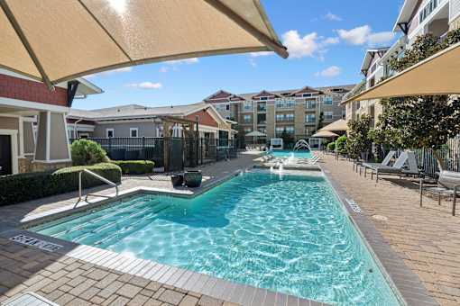 A swimming pool surrounded by a patio and apartment buildings.