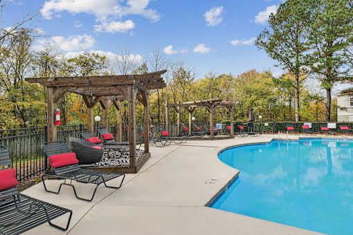 A pool area with a wooden pergola and lounge chairs.